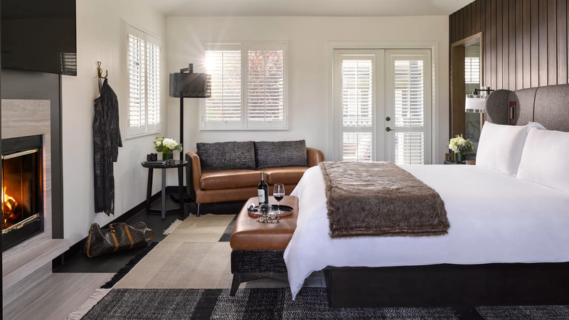 A sleek and modern guest room featured a large bed, white and dark wood paneled walls, a leather couch, and a fireplace | Hotel Yountville