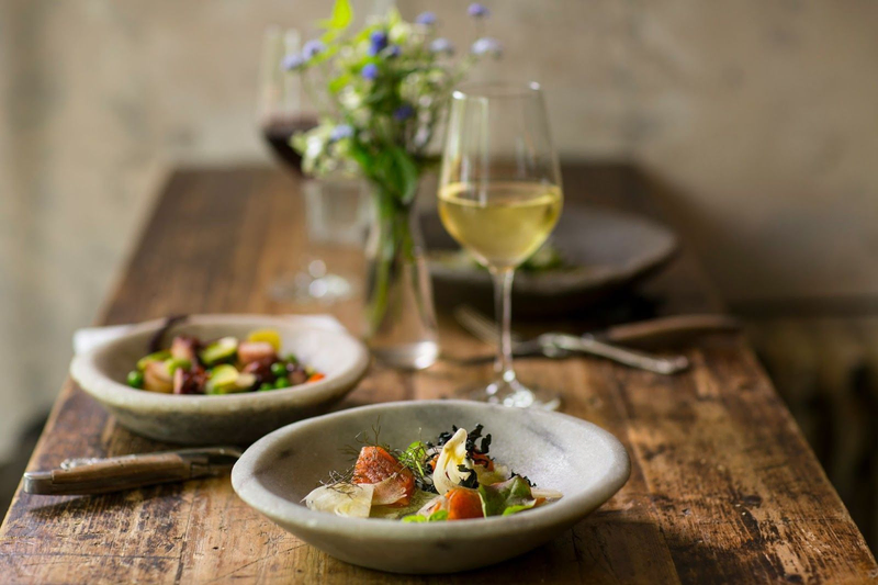 An elegantly presented meal with a glass of white wine on a rustic wooden table, complemented by a vase of flowers.