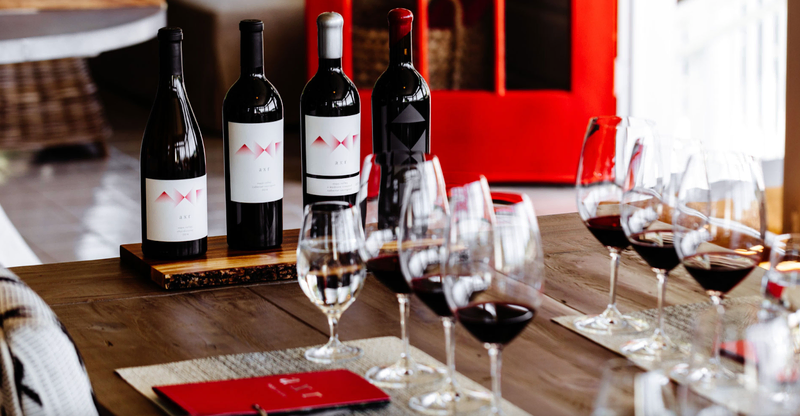 Bottles of AXR wine with multiple glasses set up for a tasting on a wooden table.