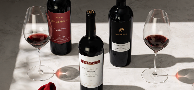 Three bottles of Louis M. Martini Cabernet Sauvignon with two glasses of red wine.