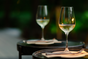 two glasses of white wine on tables in an outdoor setting.