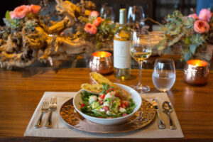 A dining table set with a salad, white wine, and elegant decor.