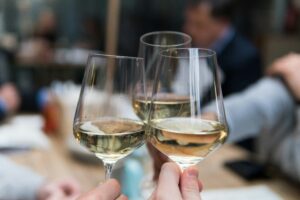 Three glasses of white wine clinking in a toast at a gathering.