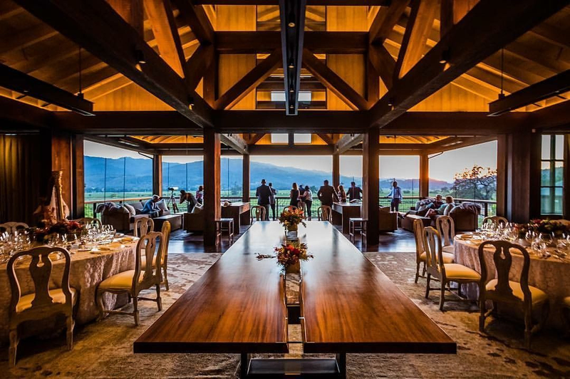 Elegant winery dining room with wooden beams, long table, and sunset vineyard view.