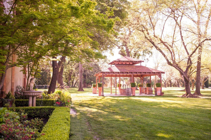 Scenic garden with a wooden gazebo surrounded by lush greenery and trees.