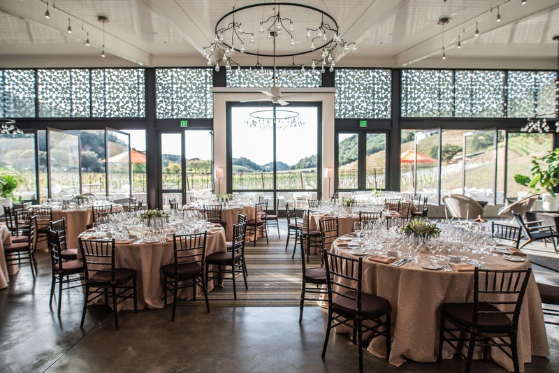 Elegant winery event space with round tables, chandeliers, and vineyard views.