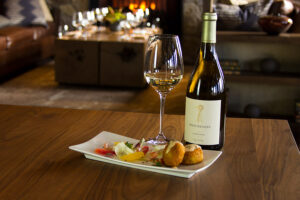 Glass of white wine with a bottle and appetizer plate on a table.