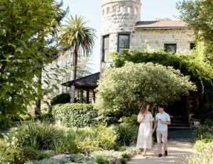 Couple walking through a lush garden near a stone tower.